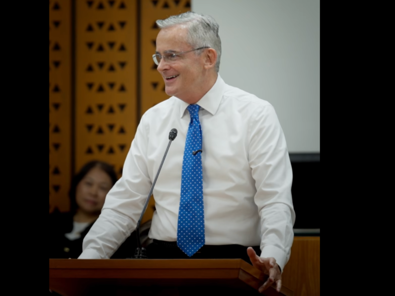 Elder Patrick Kearon smiles while speaking from a church podium.