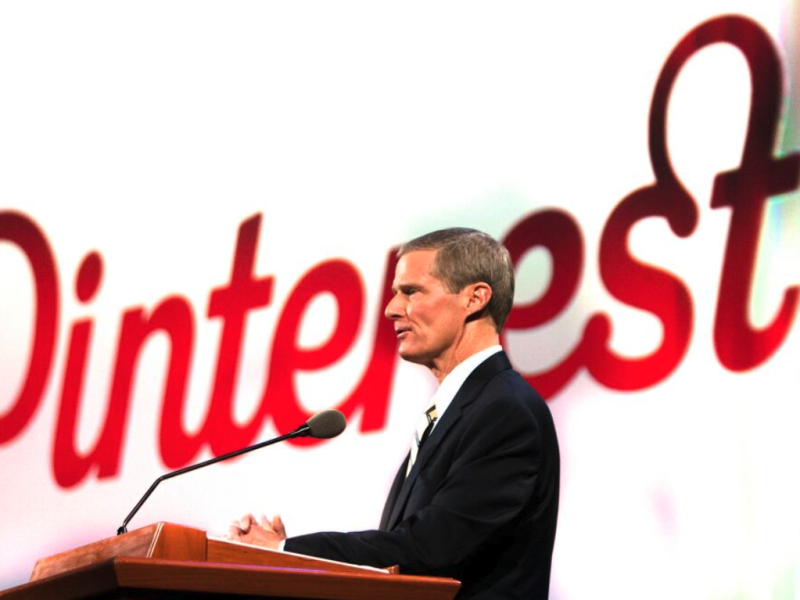 Elder David A. Bednar speaks at a pulpit in front of a projection of the Pinterest logo.