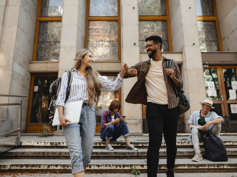 Low angle view of happy young university students greeting outdoors in front of campus. Back to university concept.