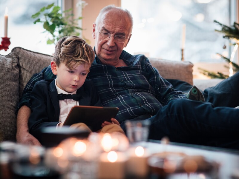 Grandfather looking at digital tablet while sitting with grandson in living room during Christmas