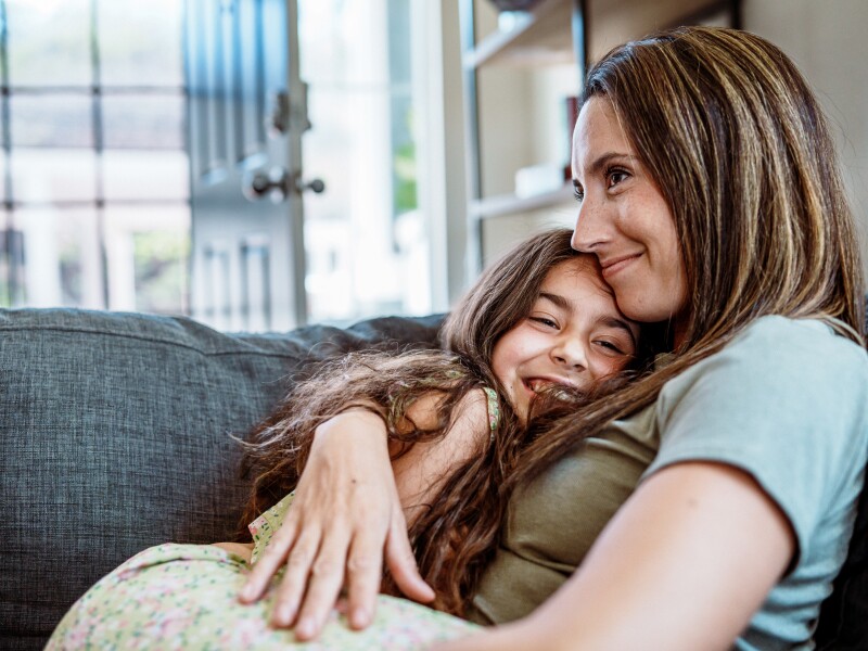 Young girl and mother hug each other on the couch