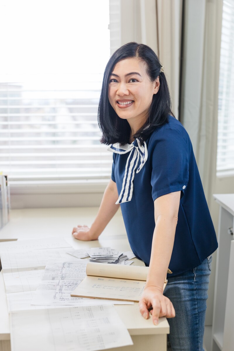 A woman smiles while leaning on a table with Taiwanese family records and temple ordinance cards.