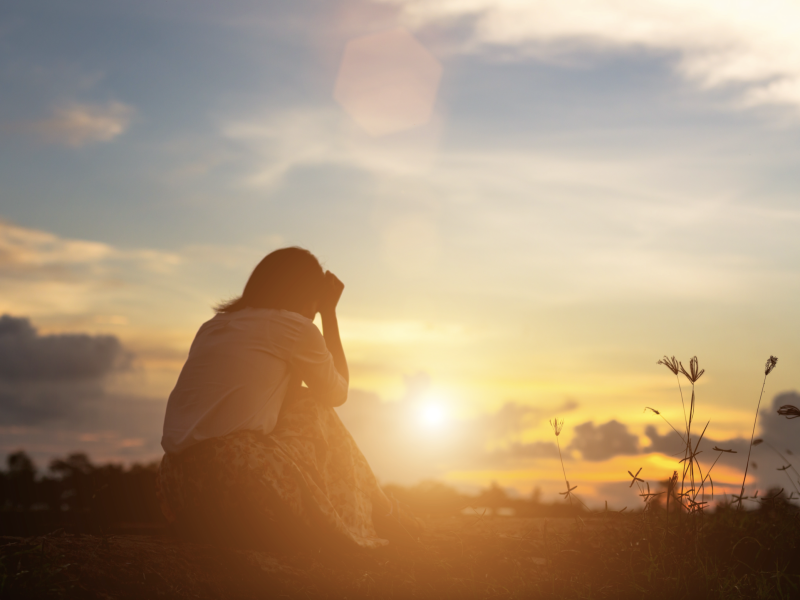 A woman kneels and looks at the sunset.