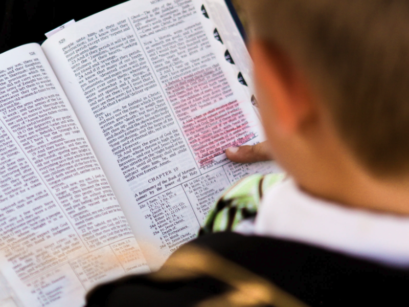 A boy holding open a copy of the Book of Mormon to Moroni chapter 10.