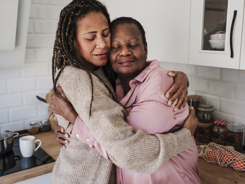 Woman with eyes closed embracing mother in kitchen at home