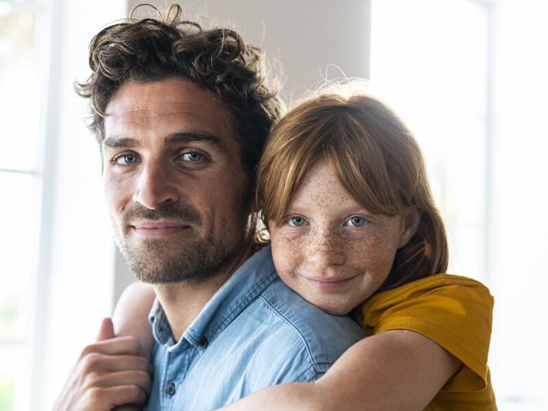 Smiling redhead daughter with blue eyes cuddling father in living room