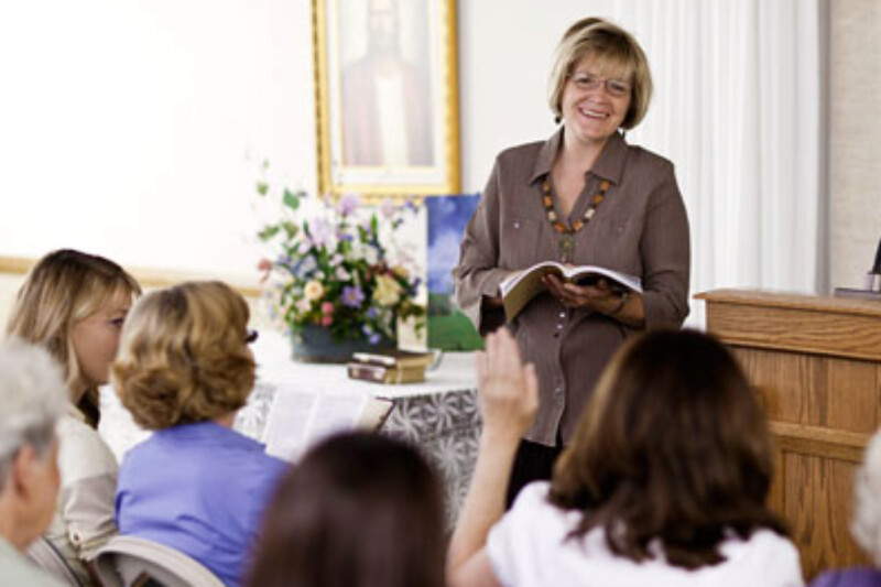 Woman teaching Relief Society smiles at a woman raising her hand in the class.