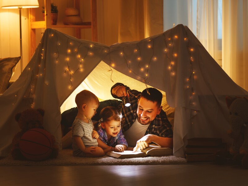happy family father and children reading a book  in  tent at home