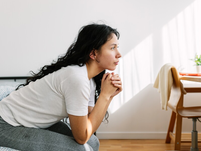 Sad and lonely thoughtful teenage girl looking away sitting on bed in the room. Social issue and adolescence bullying concept