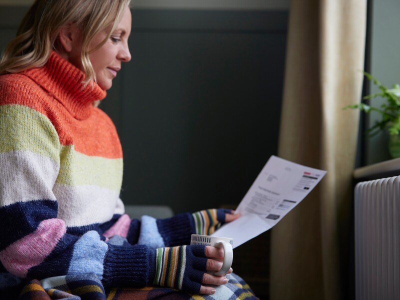 A woman holding a mug looks at a bill.