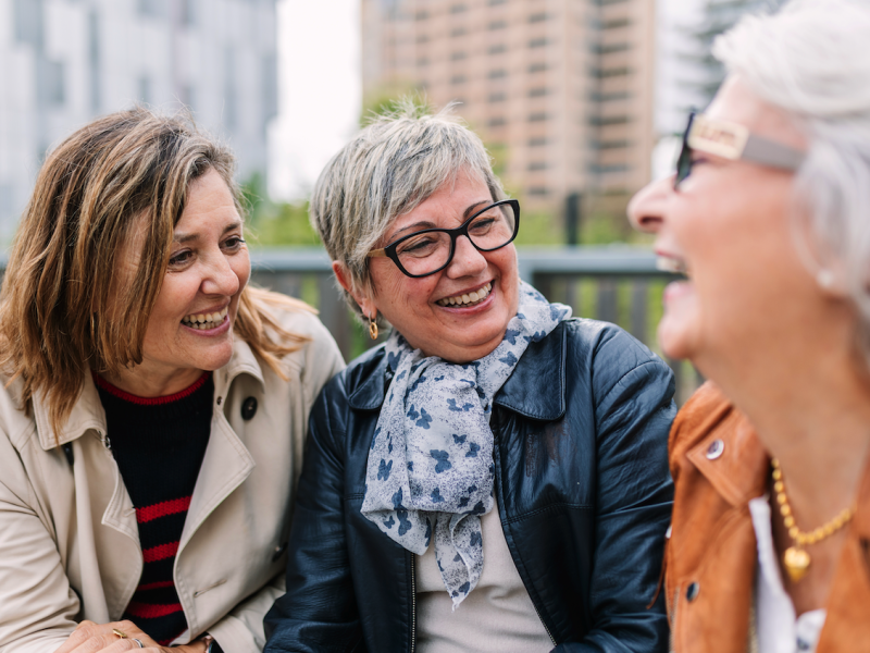 3 women sitting outside laugh together