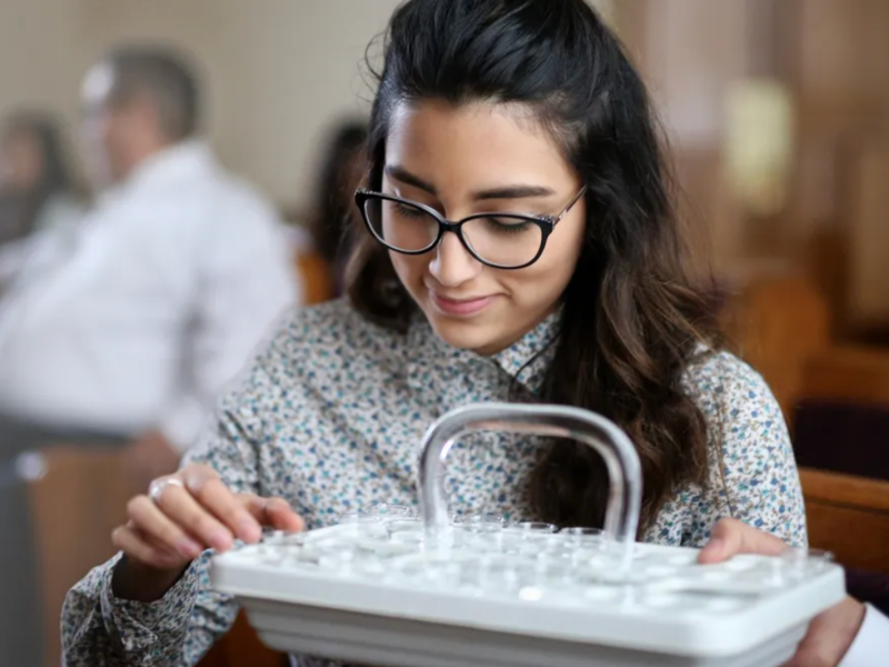 A woman holds a sacrament tray with water cups