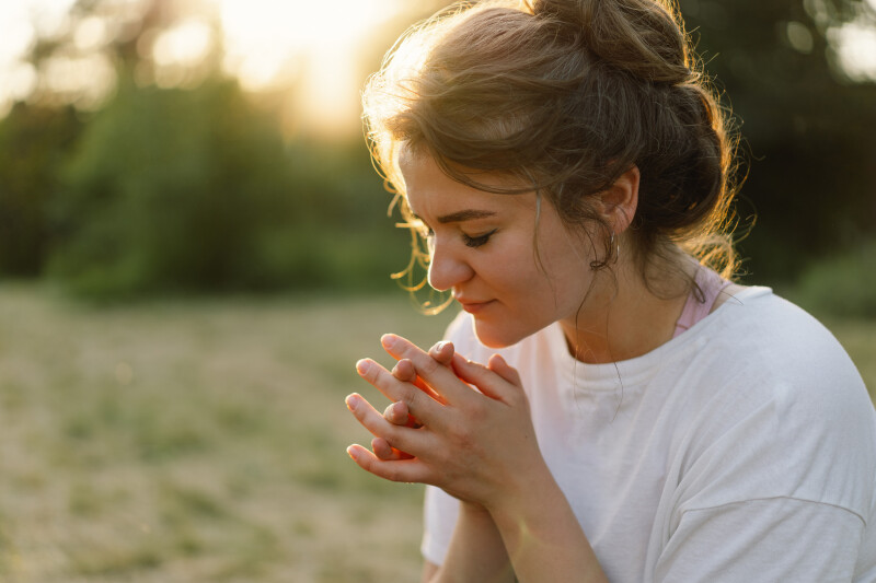A woman praying outside in a field