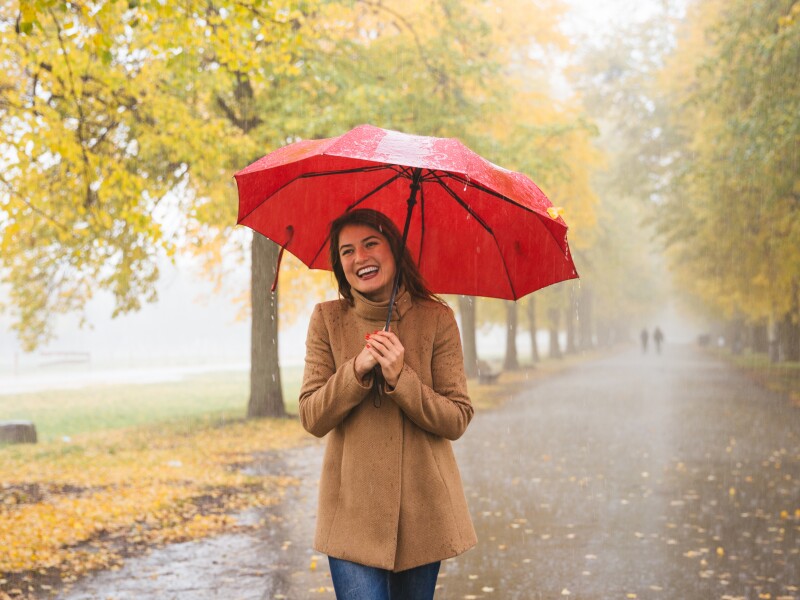 Happy woman with red umbrella walking at the rain in beautiful autumn park