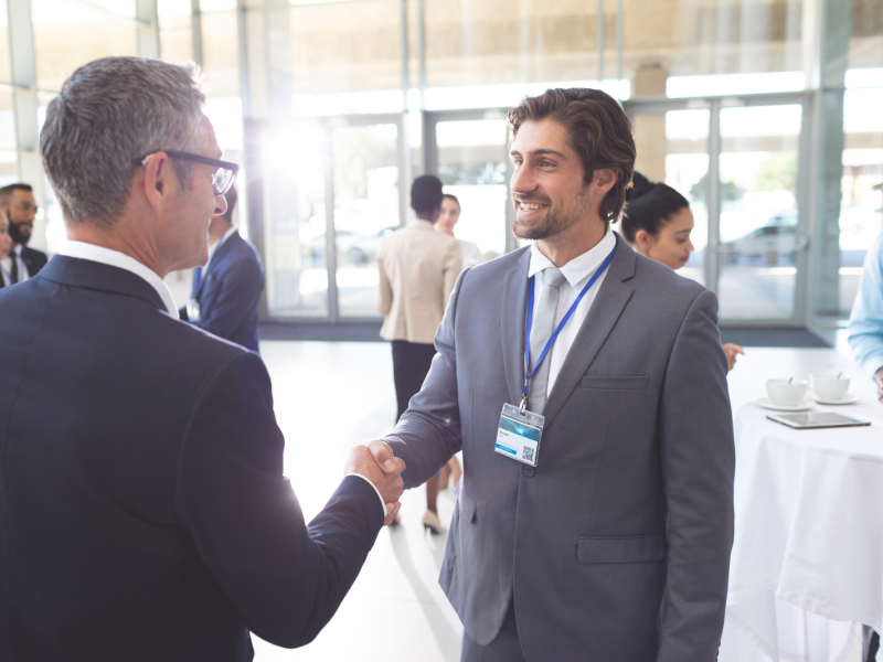 A man wearing a badge shakes another man's hand at a networking event.
