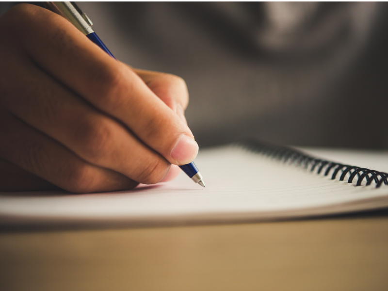 A male hand writes in a notebook with a pen