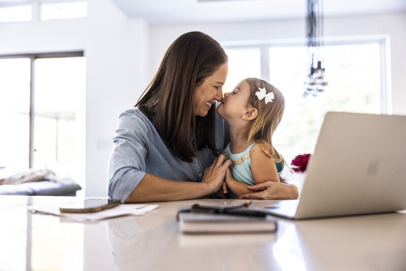 Mother working on laptop while holding toddler daughter