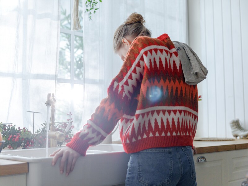 Young,Woman,In,Red,Sweater,Stays,In,Kitchen,Leaning,On