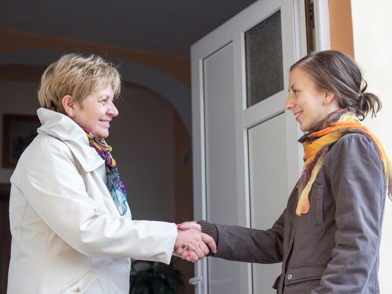 A senior woman greeting a young girl in the doorway.
