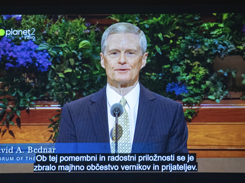 A screenshot of the April 6, 2025, PlanetTV broadcast in Slovenia of Elder David A. Bednar speaking in April 2025 general conference. The transcription of his message—in Slovenian—is “A small congregation of believers and friends gathered for this momentous and joyous occasion.”