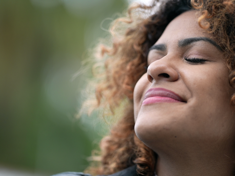 Black hispanic woman closing eyes in contemplation and smiling.