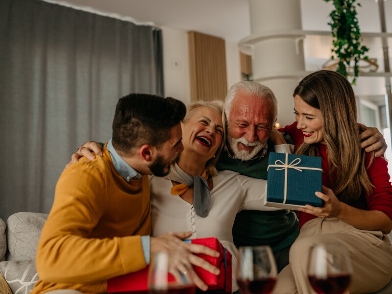 Happiness radiates from the faces of family members as they gather around a table, exchanging gifts and relishing a special Christmas lunch.