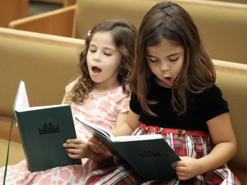 Two young girls sing from the LDS hymnbook at church