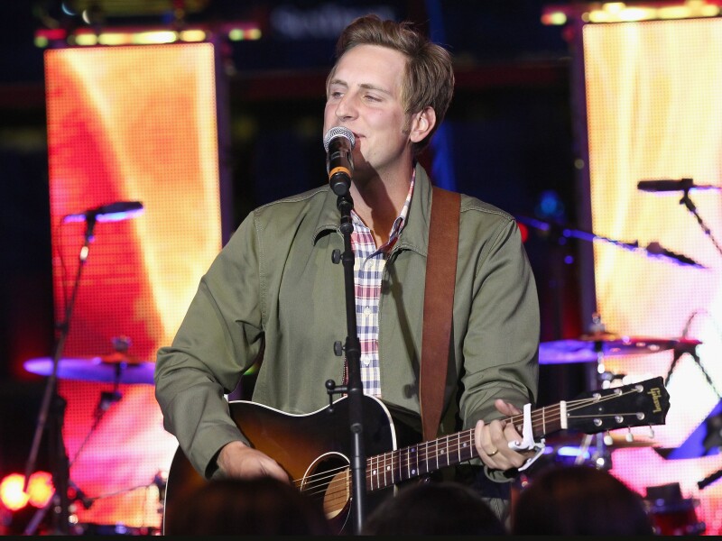 Ben Rector holds a guitar and sings on a stage.