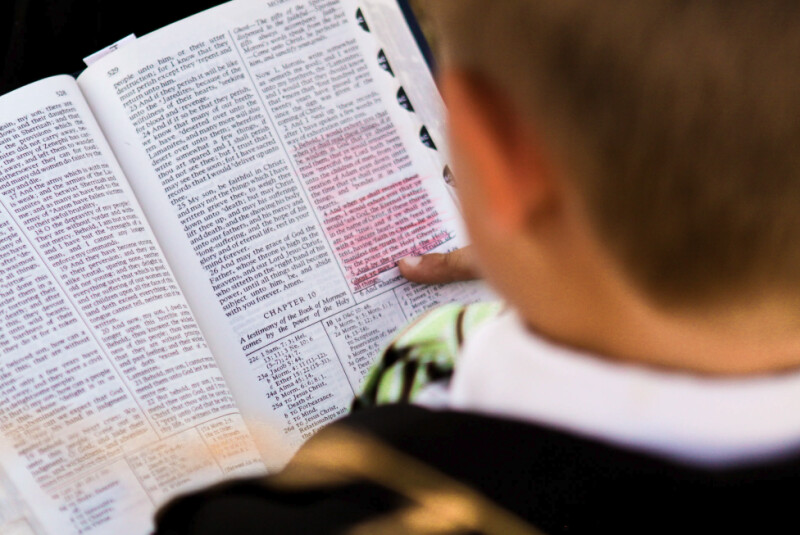 A boy holding open a copy of the Book of Mormon to Moroni chapter 10.