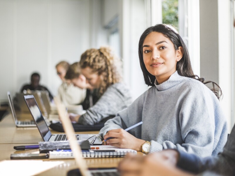 Portrait of confident young woman at desk in classroom