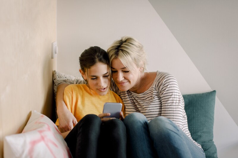 A mother and a daughter smile together looking at a phone screen.