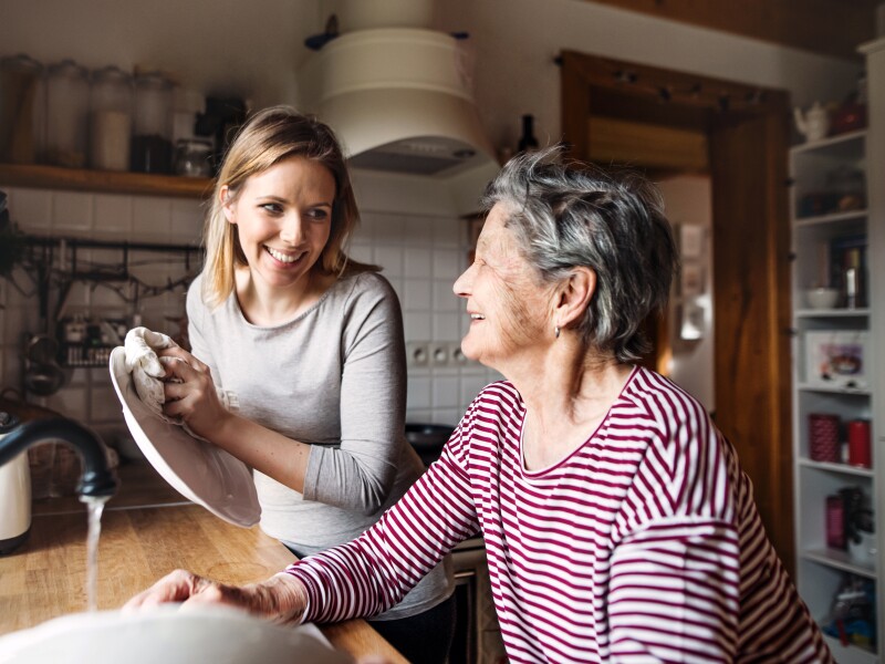 An elderly grandmother with an adult granddaughter at home, washing the dishes.