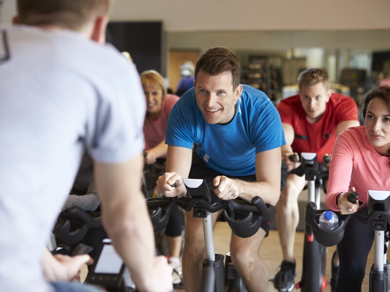 Instructor,In,Foreground,With,Spinning,Class,At,A,Gym