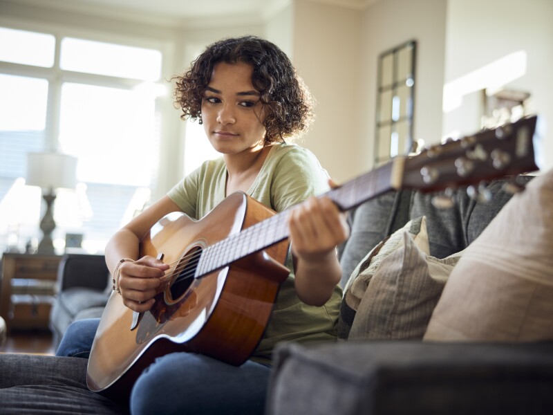 Teenage girl plays guitar on the sofa.