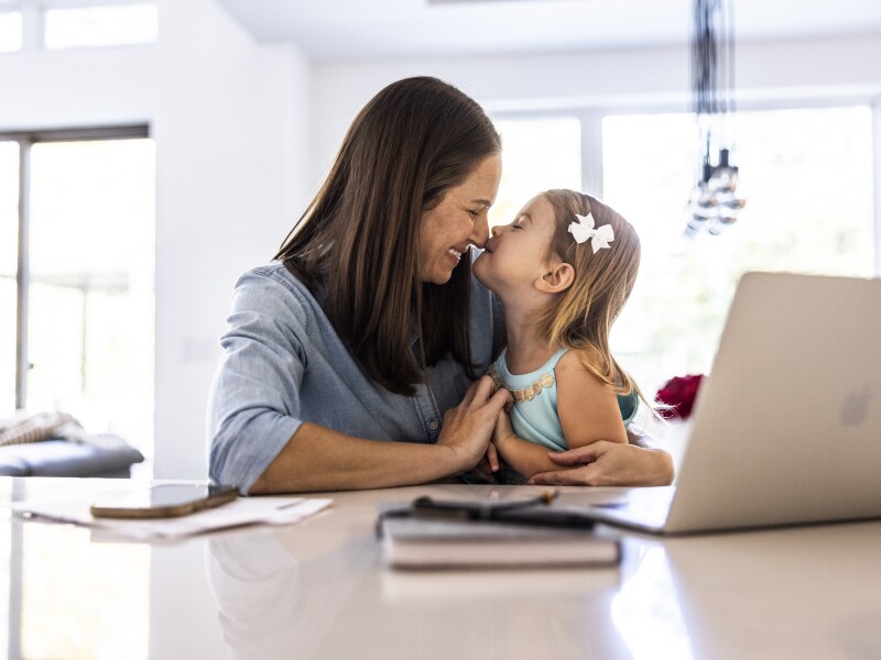 Mother working on laptop while holding toddler daughter