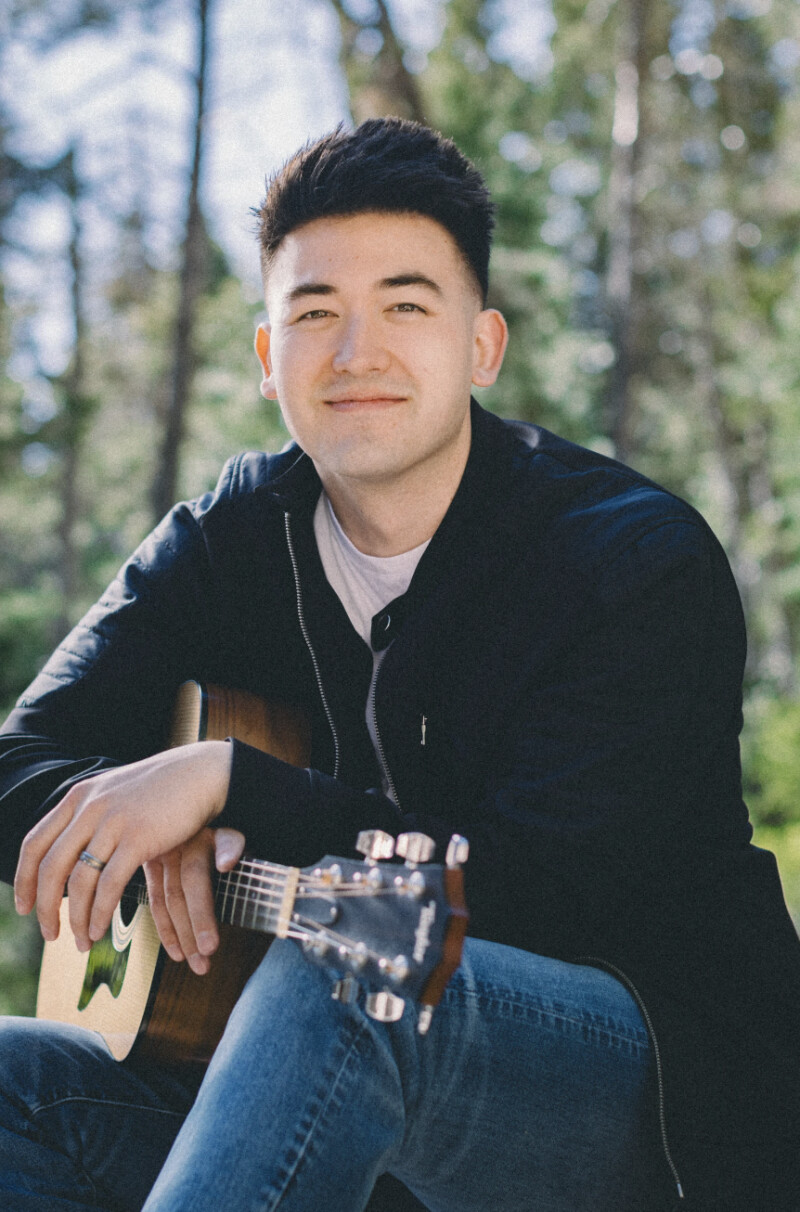 Brandon Pak smiles with a guitar.