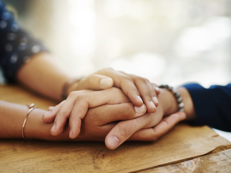 Holding hands, support and closeup with trust, solidarity and community on a home table. Therapy, diversity and gratitude of friends together with hope, respect and love for grief empathy and forgive