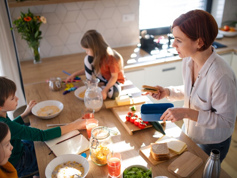 Mother of three little children preparing breakfast in kitchen at home.
