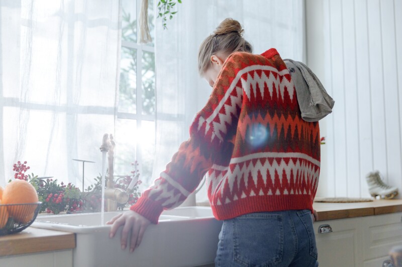 Young,Woman,In,Red,Sweater,Stays,In,Kitchen,Leaning,On