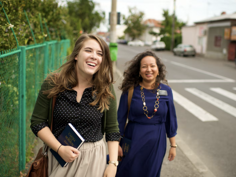 Two LDS sister missionaries in Romania laugh while walking down a street together.