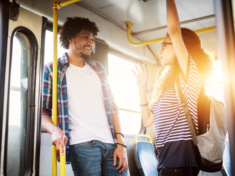 Young beautiful charming and joyful couple is standing in a bus near the doors talking and having a laugh as they travel.