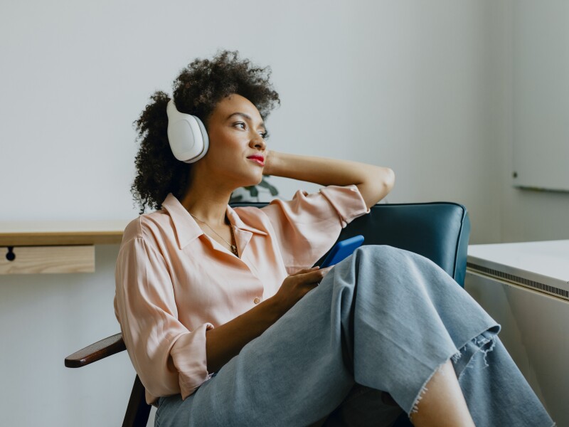 Relaxed Young Woman with Headphones on, Sitting in an Armchair and Listening to her Favorite Podcast