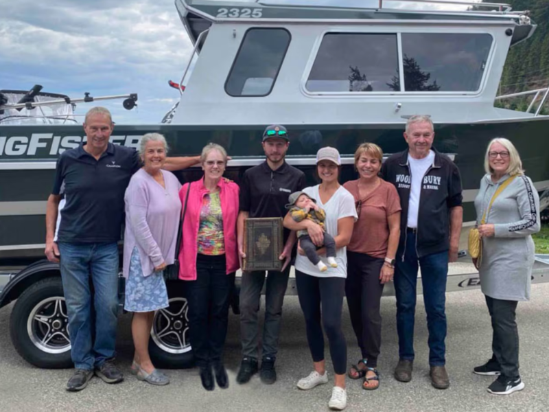 A group of eight adults and one baby pose with an heirloom Bible in front of a boat in Canada