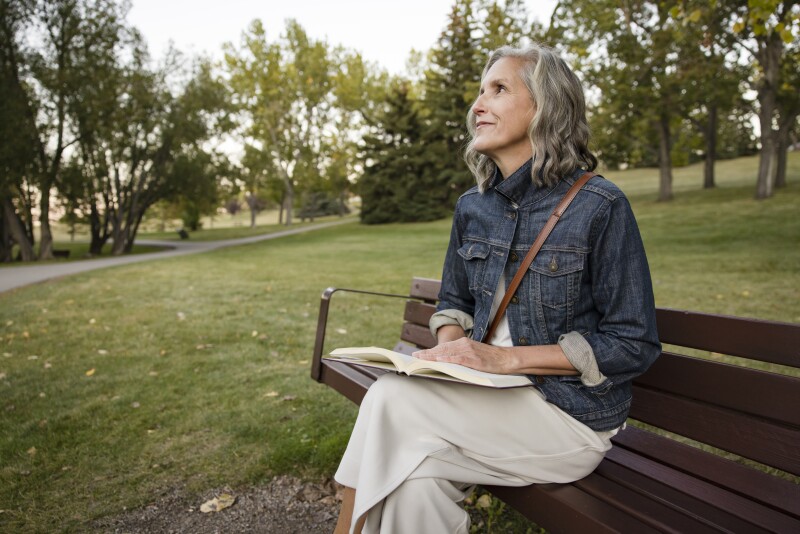 Happy senior woman reading book on park bench