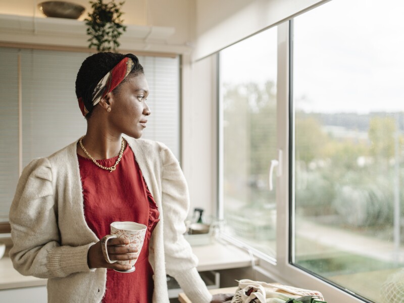 Black woman thinking and looking out the kitchen window.