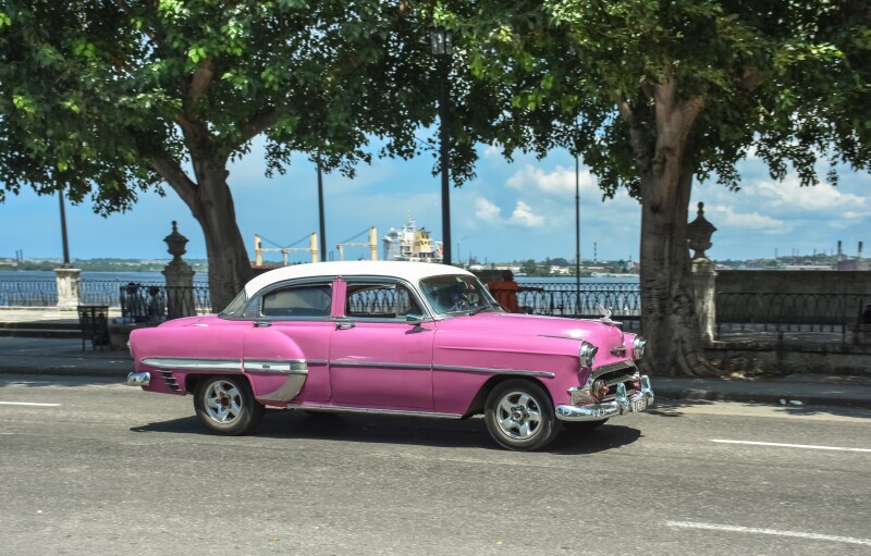 Real Cuban city life image with a pink vintage car riding by Havana's harbor