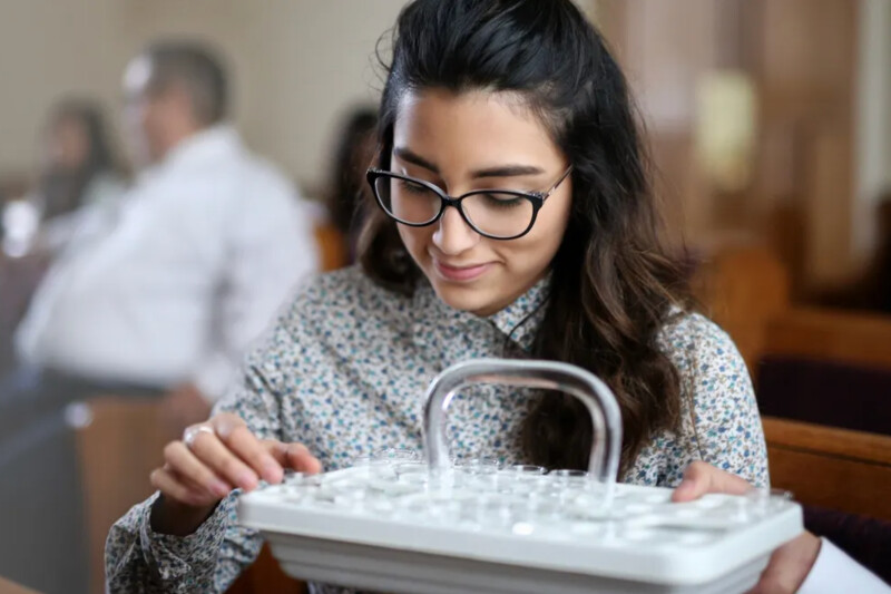 A woman holds a sacrament tray with water cups