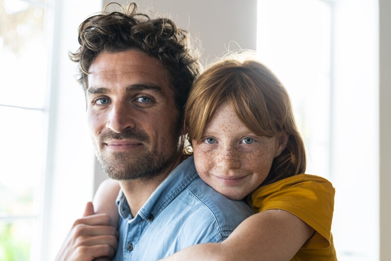 Smiling redhead daughter with blue eyes cuddling father in living room