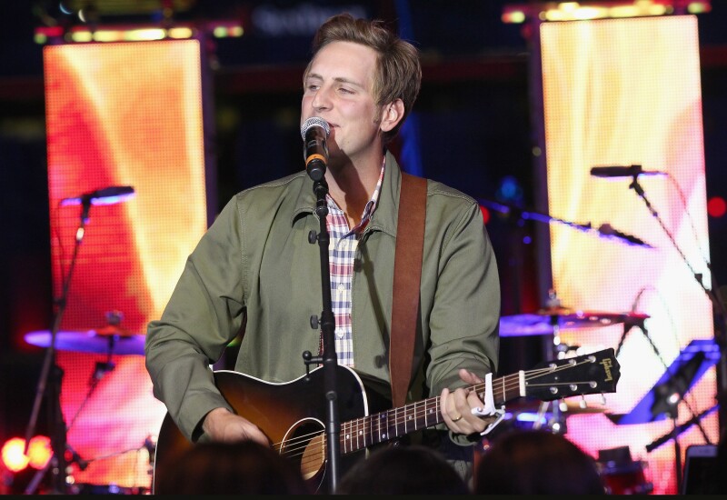 Ben Rector holds a guitar and sings on a stage.