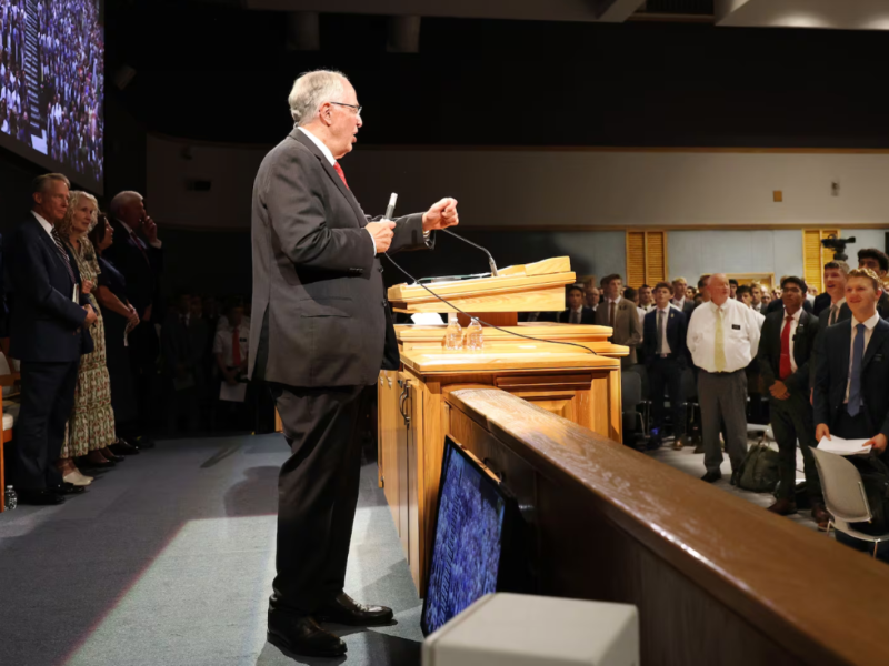 Elder Neil L. Andersen stands beside a microphone podium at the Provo Missionary Training Center